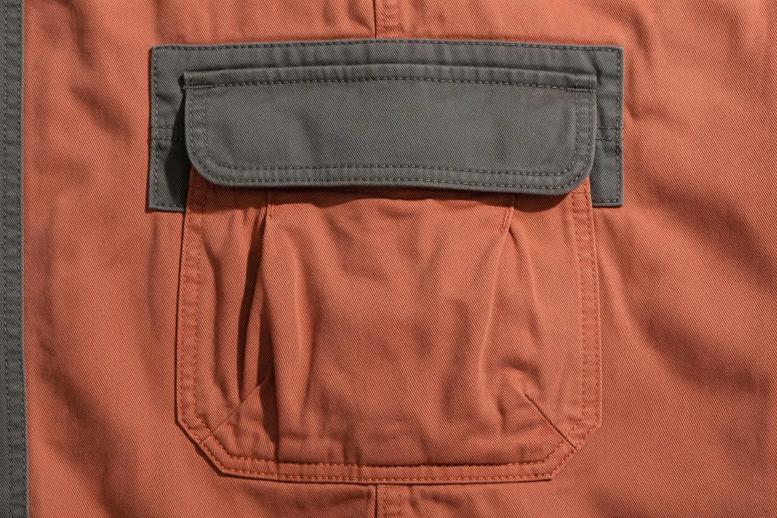 Terracotta cargo pocket detail with side folds, stitched edges and a charcoal-grey flap.