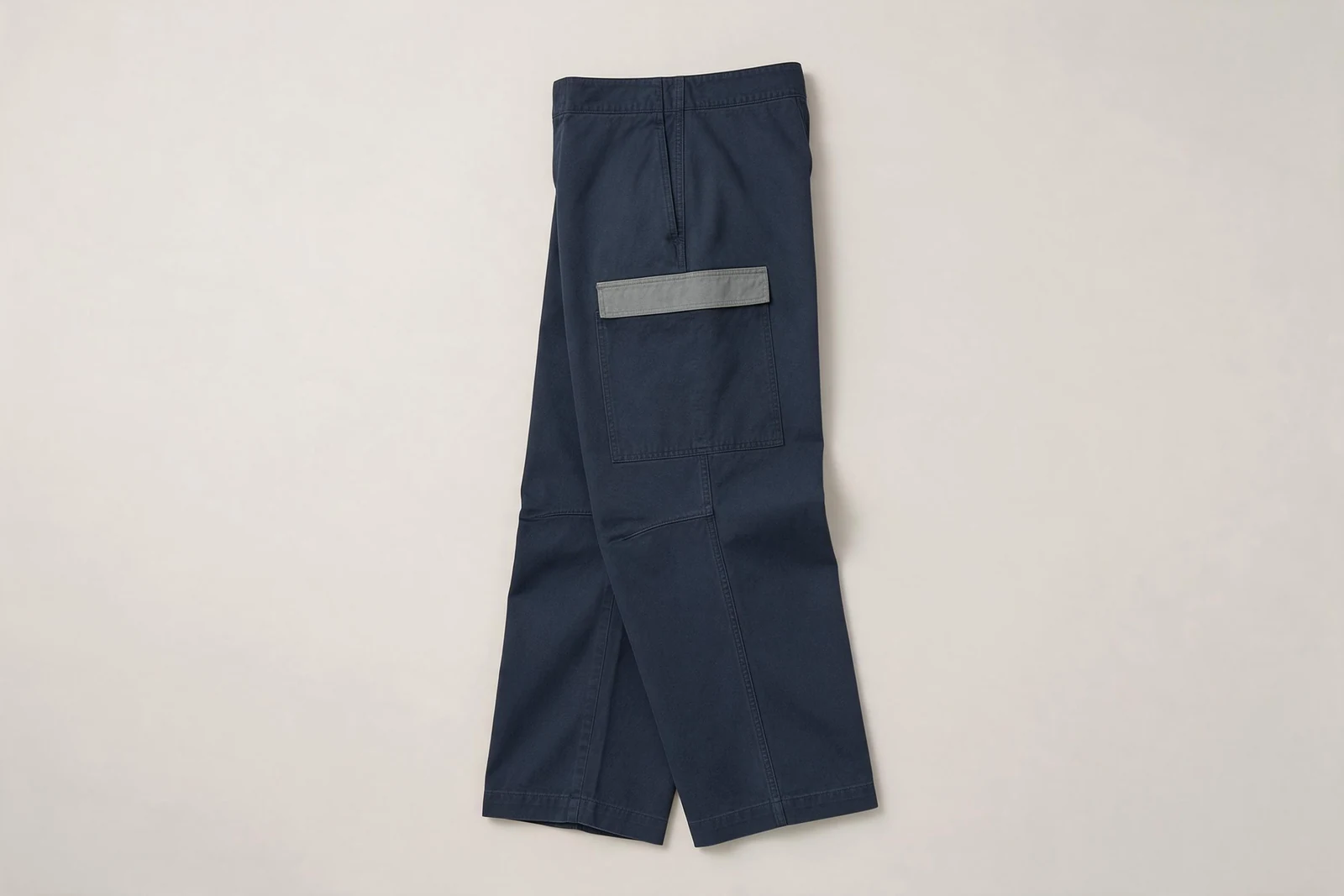 Navy cargo pants folded to show a side pocket with a grey flap above a curved leg seam.