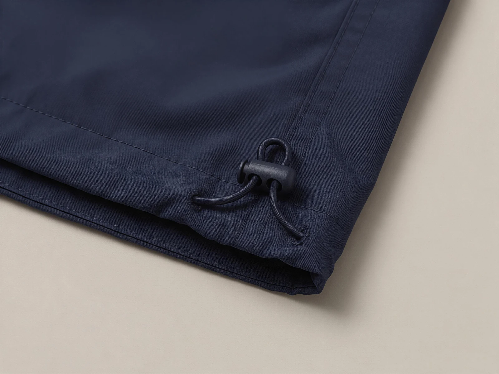 A navy jacket hem corner with two cord exits and a black cord lock.
