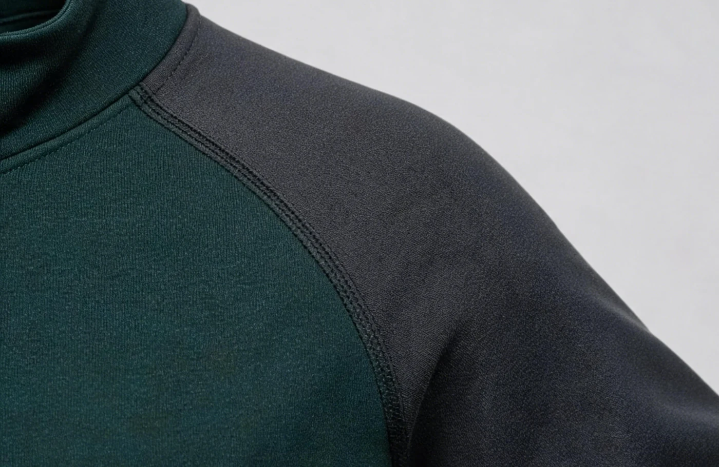 Diagonal seam detail joining a dark green body panel to a charcoal sleeve.