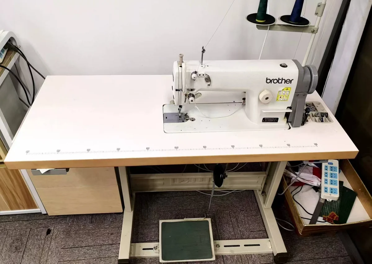 An industrial sewing workstation with a thread stand and foot pedal