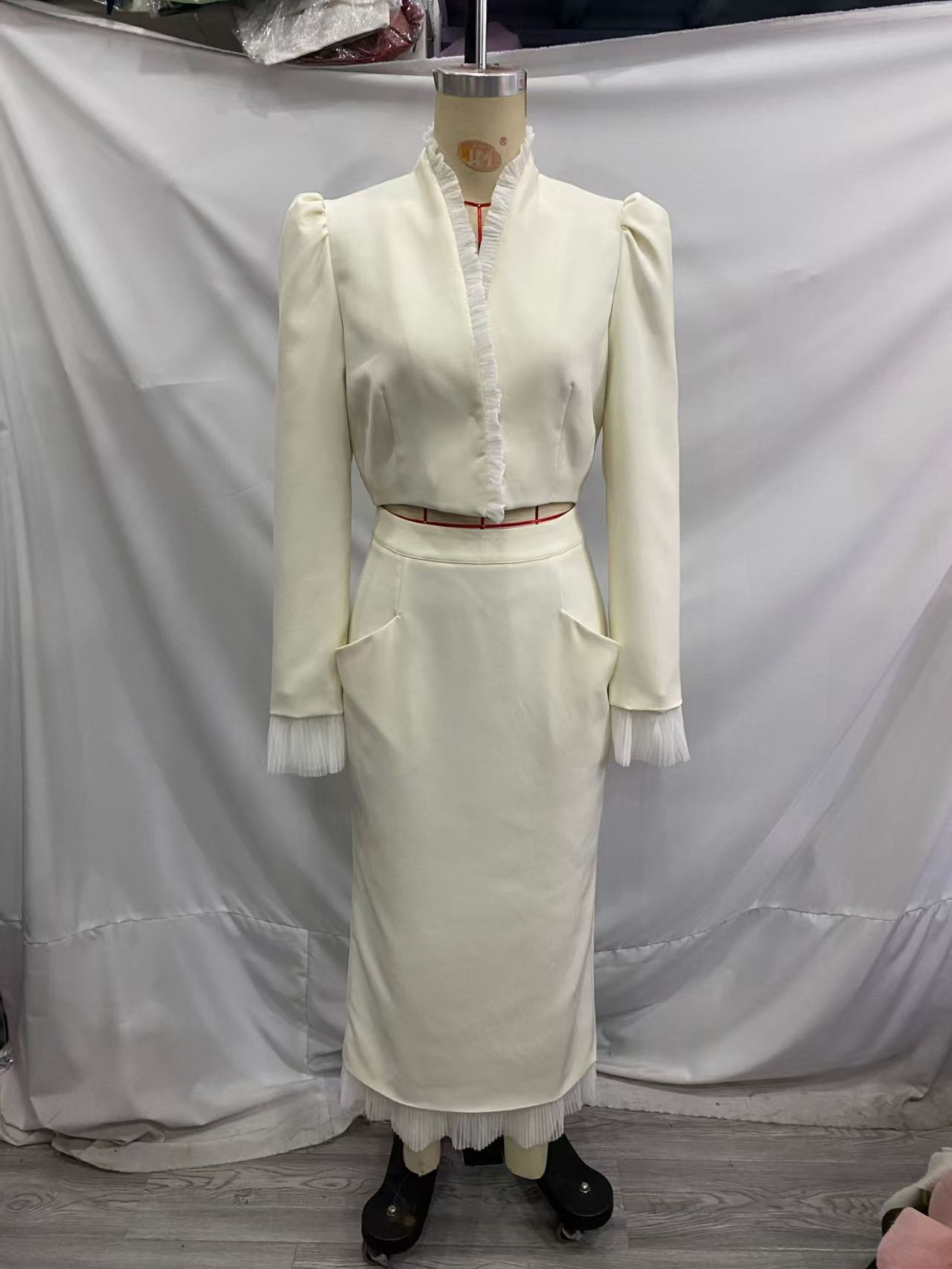 Ivory cropped jacket and long skirt displayed on a dress form, with shaped skirt pockets and pleated trim.