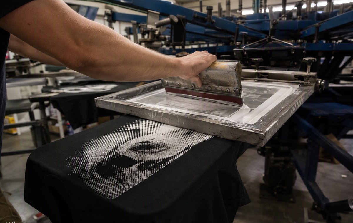 Screen printing press applying ink through a mesh screen onto a t-shirt